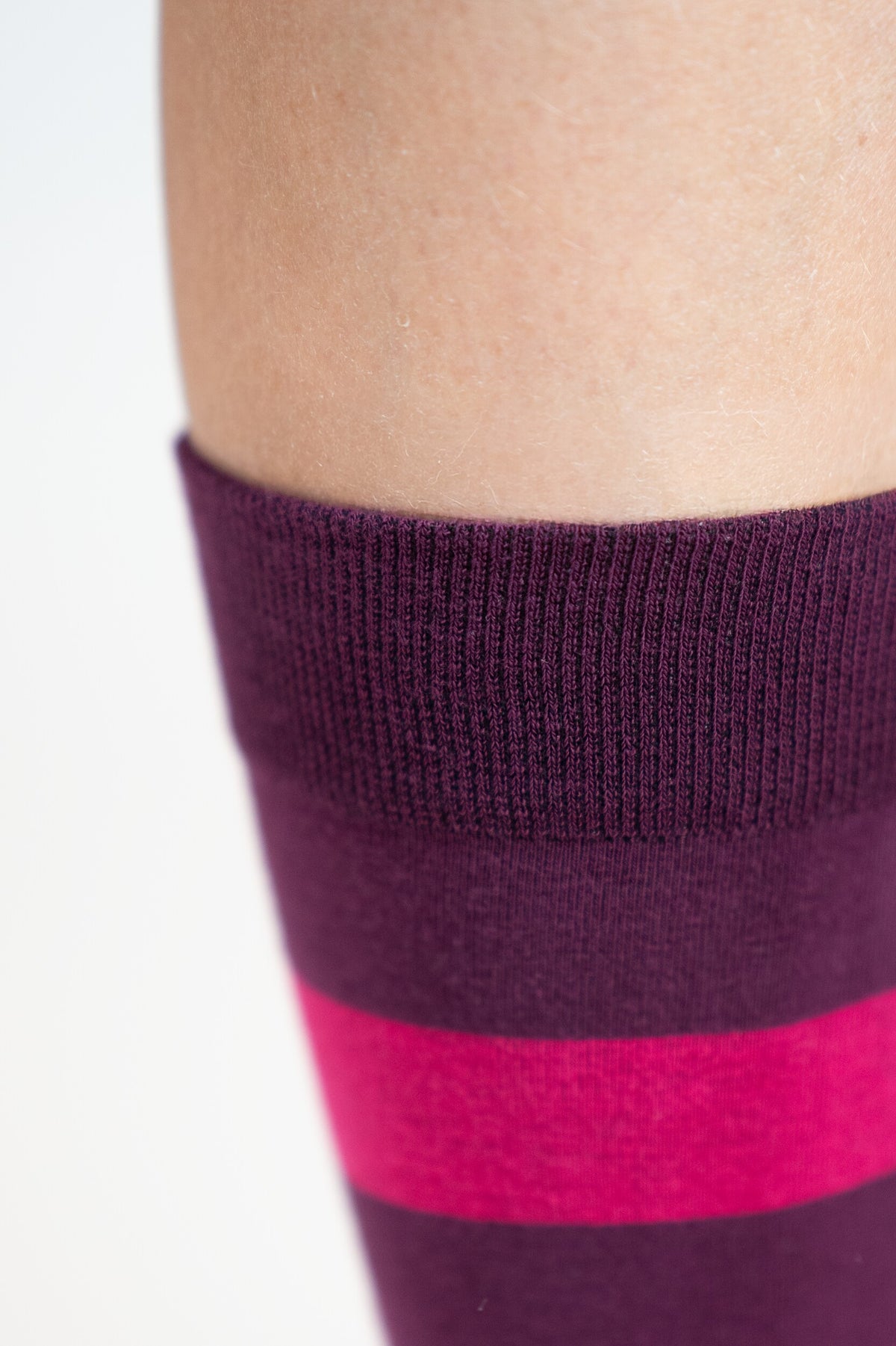 Nahaufnahme des Komfortbunds am oberen Rand des Kniestrumpfs mit Ringelmuster in Pink und Dunkelviolett, am Bein getragen.