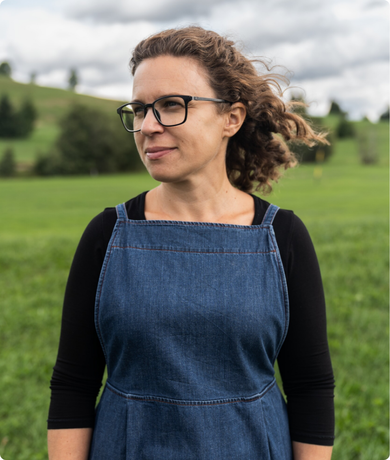 Portrait von Isabel, Gründerin von Ringel Days, im Jeans-Latzkleid vor grüner Wiesenlandschaft, Haare im Wind, Blick zur Seite.