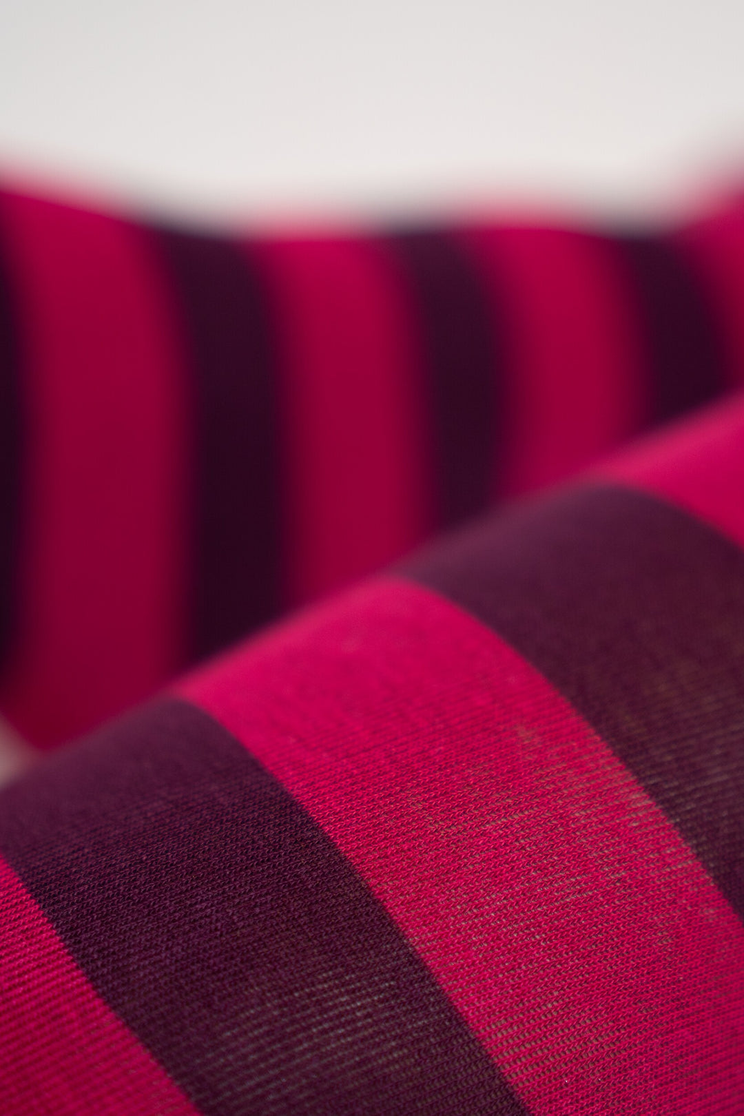 Nahaufnahme des gestrickten Ringel-Musters in Pink und Dunkelviolett aus Bio-Baumwolle, Detailaufnahme der Strickstruktur.
