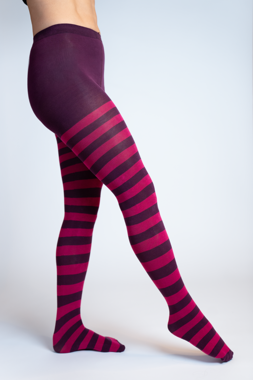 Strumpfhose mit dunkelviolettem Bund und Ringelmuster in Pink und Dunkelviolett, Bein nach vorne gestreckt mit aufgesetzter Fussspitze, auf hellem Hintergrund.