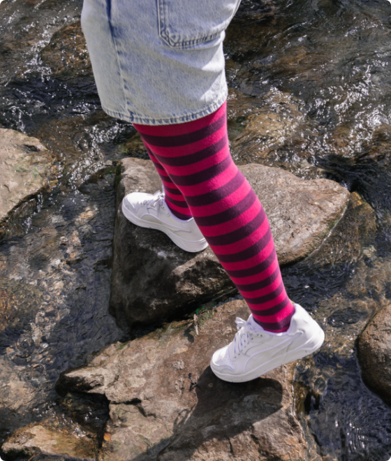 Person hält einen Blumenstrauss in der Hand, trägt schwarze Schnürstiefel und eine geringelte Strumpfhose in Pink und Dunkelviolett.